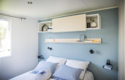 Camera moderna con parete blu, biancheria bianca e scaffali allo Starcaravan Lavaurette, Les 3 Cantons.