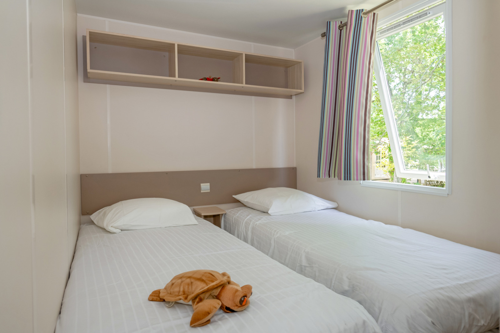 Slaapkamer met twee eenpersoonsbedden, wit beddengoed, knuffel en raam in Mobile home «Midi Pyrénées».