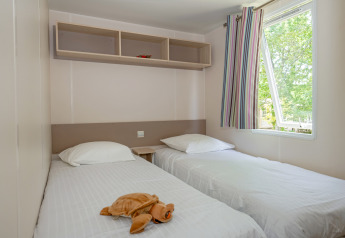 Bedroom with two single beds, white linens, a plush toy, and window at Mobile home «Midi Pyrénées».