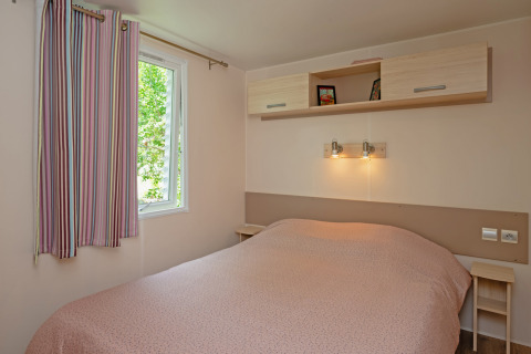 Dormitorio del Mobile home «Midi Pyrénées» en el camping Les 3 Cantons en Francia, con cama doble y ventana.