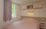 Dormitorio del Mobile home «Midi Pyrénées» en el camping Les 3 Cantons en Francia, con cama doble y ventana.
