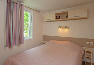 Camera da letto nel Mobile home «Midi Pyrénées» al campeggio Les 3 Cantons in Francia con letto matrimoniale.