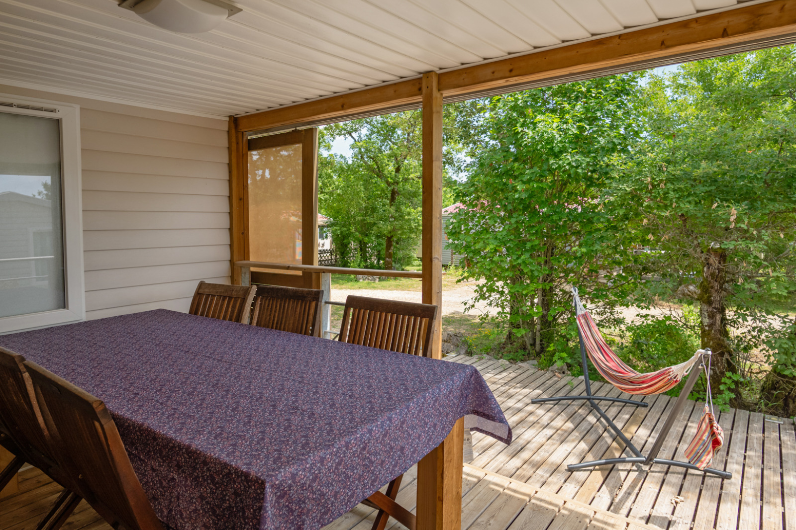 Overdekt terras bij Mobile home «Midi Pyrénées» op Camping Les 3 Cantons met eettafel en hangmat.
