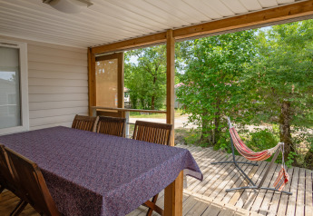 Covered terrace at Mobile home “Midi Pyrénées” at Campsite Les 3 Cantons with dining table and hammock.