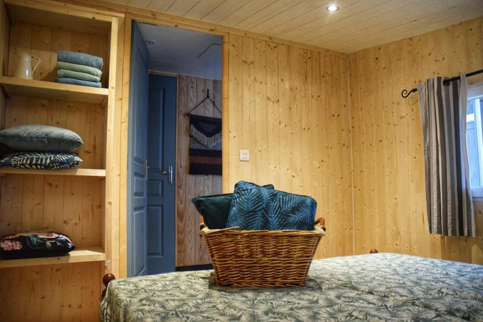 Slaapkamer in lodge 'Upupa' op Camping Les 3 Cantons, Frankrijk, met houten muren en mand op bed.