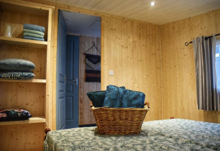 Dormitorio en la cabaña 'Upupa' del camping Les 3 Cantons, Francia, con paredes de madera y cesta en la cama.