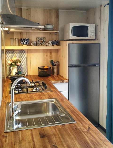 Pequeña cocina moderna en la cabaña Upupa del camping Les 3 Cantons, encimera de madera y microondas.
