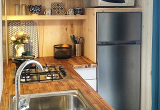 Pequeña cocina moderna en la cabaña Upupa del camping Les 3 Cantons, encimera de madera y microondas.