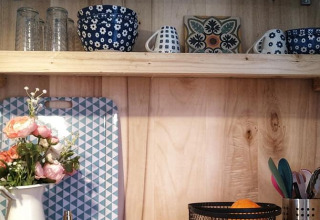 Acogedora cocina pequeña con estantes de madera, vajilla azul, cesta de frutas y jarra con flores.