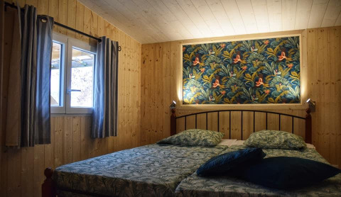 Dormitorio acogedor en la cabaña Upupa del camping Les 3 Cantons, Francia, con paredes de madera y arte colorido.