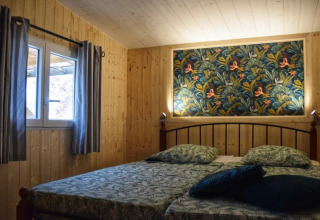 Dormitorio acogedor en la cabaña Upupa del camping Les 3 Cantons, Francia, con paredes de madera y arte colorido.