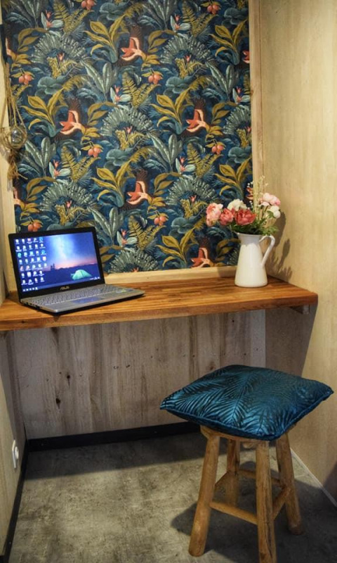 Acogedor rincón de trabajo con portátil y jarra de flores en la lodge Upupa, Campsite Les 3 Cantons, Francia.
