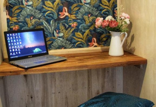 Acogedor rincón de trabajo con portátil y jarra de flores en la lodge Upupa, Campsite Les 3 Cantons, Francia.