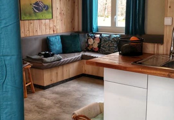 Gemütlicher Wohnbereich in der Lodge 'Upupa' auf dem Campingplatz Les 3 Cantons mit Sofa und Küche.