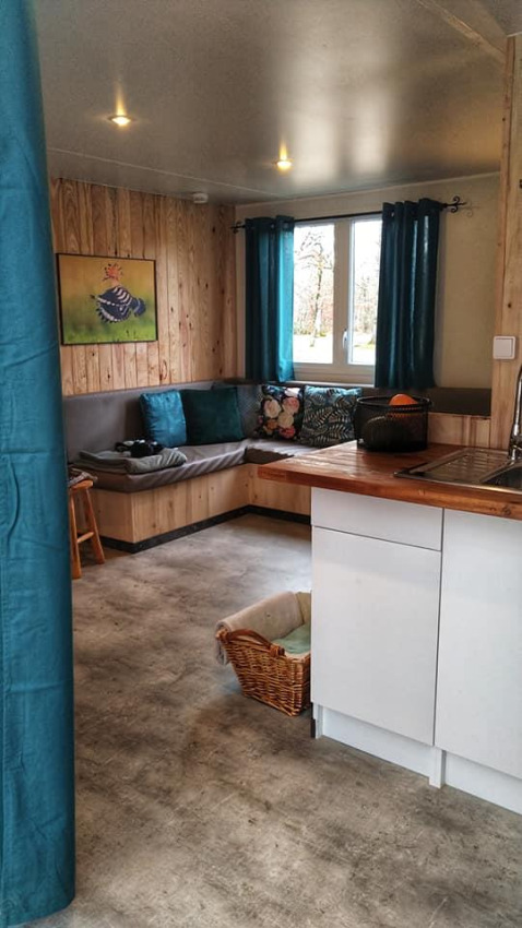 Acogedora sala de la cabaña Upupa en el camping Les 3 Cantons, Francia, con sofá, cocina y ventana.