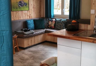 Cozy living area inside Upupa lodge at Campsite Les 3 Cantons, France, featuring wood, sofa, and kitchen.