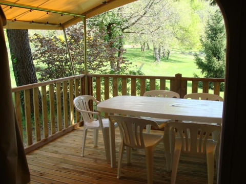Houten terras bij safaritent met plastic tafel en stoelen, zicht op groene natuur en bomen buiten.