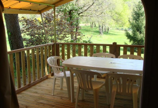 Houten terras bij safaritent met plastic tafel en stoelen, zicht op groene natuur en bomen buiten.