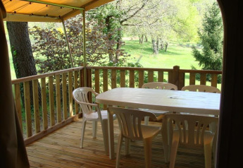 Veranda in legno di tenda safari con tavolo e sedie di plastica, vista su alberi e prato verdi.