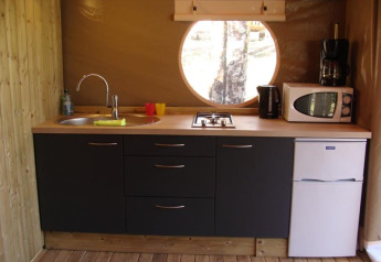 Cuisine moderne de tente safari au Lodge Canada Comfort en France, avec évier, plaque, micro-ondes et fenêtre ronde.