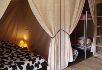 Interno di tenda safari con letto matrimoniale, letti a castello, luce soffusa e mensole visibili.