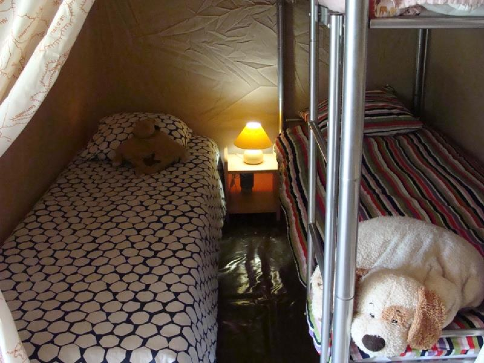 Interieur van het Lodge Canada Comfort safaritent met eenpersoonsbed, stapelbed, nachtkastje en lamp.