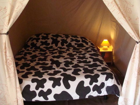 Interno di una tenda safari con letto dalla coperta bianco-nera e un piccolo comodino con lampada.