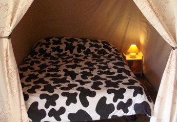 Interno di una tenda safari con letto dalla coperta bianco-nera e un piccolo comodino con lampada.