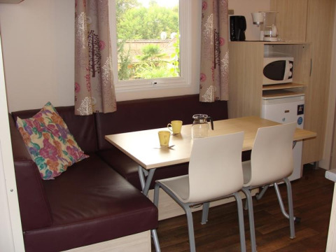 Coin repas avec table, chaises et banquette dans le Mobile home Comfort au camping La Grande Véyière en France.