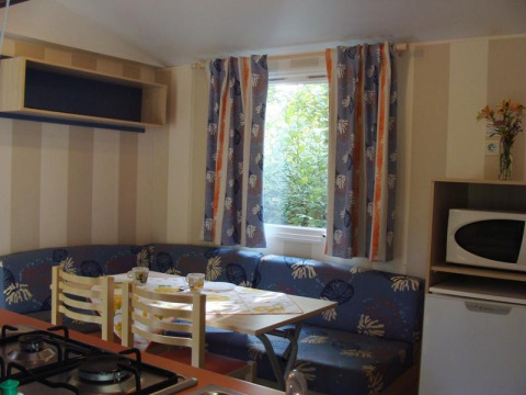 Interior of a mobile home with dining table, corner sofa, fridge, and microwave at Campsite La Grande Véyière.