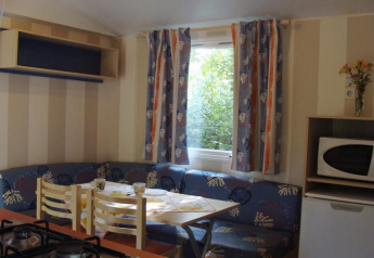 Interior of a mobile home with dining table, corner sofa, fridge, and microwave at Campsite La Grande Véyière.