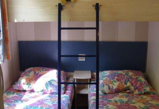 Mobile home bedroom with bunk bed, floral bedding on twin beds, and a teddy bear on the upper bunk.