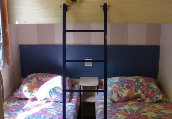 Zimmer in einem Mobilheim mit zwei Einzelbetten, bunter Bettwäsche und Kuscheltier auf dem Hochbett.