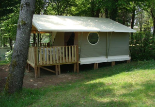 Tenda safari Lodge «Canada Classic» con veranda in legno al Campeggio La Grande Véyière in Francia, tra gli alberi.
