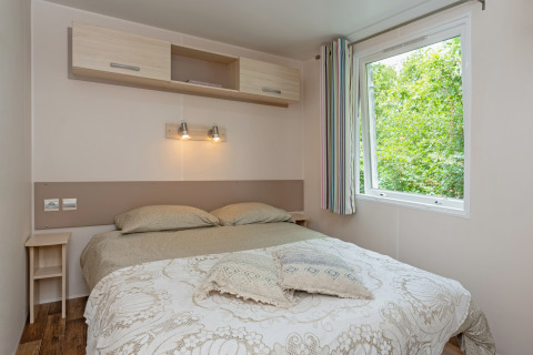 Chambre du Mobile home «Loggia» au Camping Les 3 Cantons en France, avec lit double et fenêtre sur la nature.