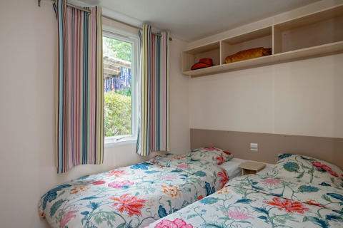Zimmer mit zwei Einzelbetten, bunten Blumenbettdecken, gestreiften Vorhängen und Regalen im Mobile home Loggia.