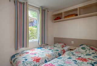 Værelse med to enkeltsenge, farverige blomstersenge, stribede gardiner og hylder på Mobile home Loggia.