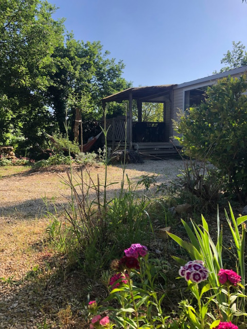 Vista soleada del mobile home «Loggia» en el camping Les 3 Cantons, Francia, con flores y vegetación alrededor.