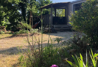 Vue ensoleillée du Mobile home «Loggia» au camping Les 3 Cantons en France, entouré de verdure et de fleurs.
