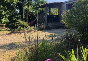 Sunny view of Mobile home «Loggia» at Campsite Les 3 Cantons in France, surrounded by lush greenery and flowers.