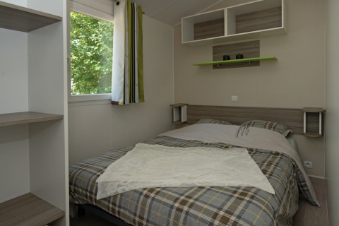 Soveværelse i Mobile home «Aveyron» på Campsite Les 3 Cantons, Frankrig, med dobbeltseng og udsigt til træer.