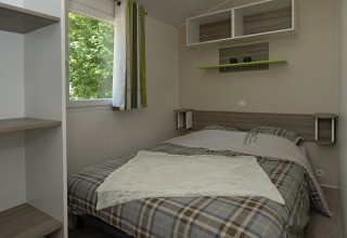 Chambre du Mobil-home «Aveyron» au Camping Les 3 Cantons en France, avec un lit double et vue sur les arbres.