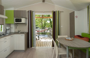 Intérieur de mobil-home moderne avec cuisine, table à manger et terrasse avec hamac en extérieur.