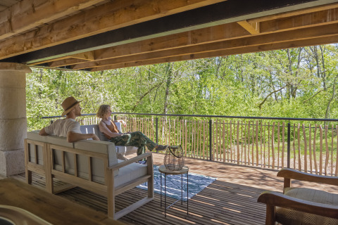 Twee mensen ontspannen op het terras van de Duiventoren-boomhut op Camping Les 3 Cantons, Frankrijk.