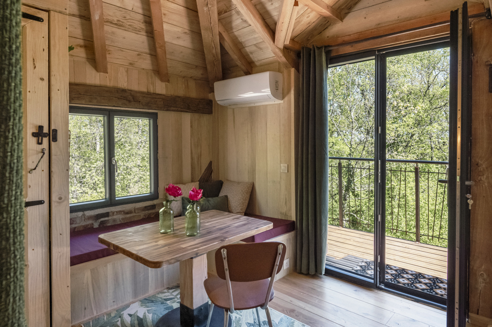 Knus boomhuisinterieur met houten balken, tafel, zitbank en balkon bij Les 3 Cantons in Frankrijk.