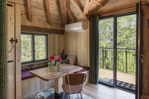Knus boomhuisinterieur met houten balken, tafel, zitbank en balkon bij Les 3 Cantons in Frankrijk.