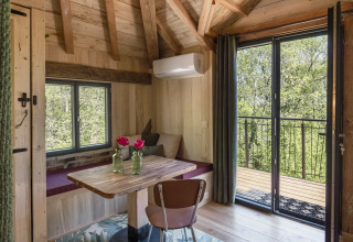 Knus boomhuisinterieur met houten balken, tafel, zitbank en balkon bij Les 3 Cantons in Frankrijk.