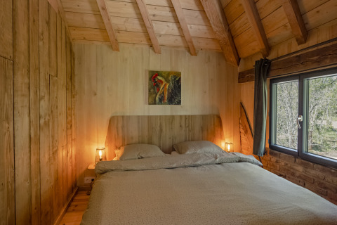 Slaapkamer in boomhut 'Duiventoren' op Camping Les 3 Cantons in Frankrijk met een comfortabel tweepersoonsbed.