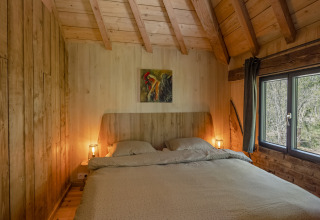 Slaapkamer in boomhut 'Duiventoren' op Camping Les 3 Cantons in Frankrijk met een comfortabel tweepersoonsbed.