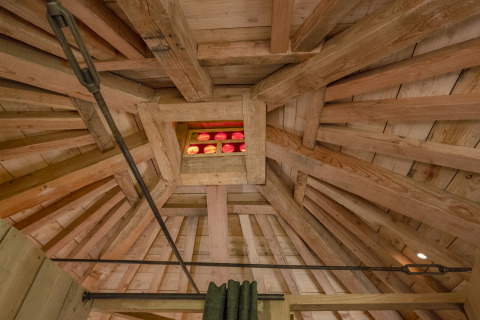 Houten balkenplafond met klein kleurrijk raam in boomhut 'Duiventoren' op Camping Les 3 Cantons, Frankrijk.